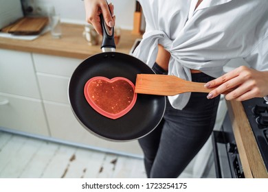 Homemade Woman Likes To Cook Delicious Desserts From Natural Products. Making Banana Pancakes, Turning Over By Wooden Spatula The Already Fried Side Of The Fritters In The Pan. Heart And Star Pancakes