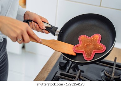 Homemade Woman Likes To Cook Delicious Desserts From Natural Products. Making Banana Pancakes, Turning Over By Wooden Spatula The Already Fried Side Of The Fritters In The Pan. Heart And Star Pancakes