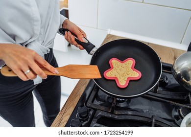 Homemade Woman Likes To Cook Delicious Desserts From Natural Products. Making Banana Pancakes, Turning Over By Wooden Spatula The Already Fried Side Of The Fritters In The Pan. Heart And Star Pancakes