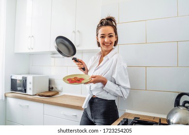 Homemade Woman Likes To Cook Delicious Desserts From Natural Products. Making Banana Pancakes, Turning Over By Wooden Spatula The Already Fried Side Of The Fritters In The Pan. Smiling, Feeling Happy