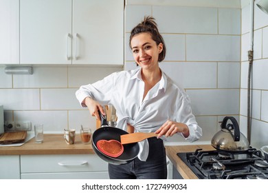 Homemade Woman Likes To Cook Delicious Desserts From Natural Products. Making Banana Pancakes, Turning Over By Wooden Spatula The Already Fried Side Of The Fritters In The Pan. Heart And Star Pancakes