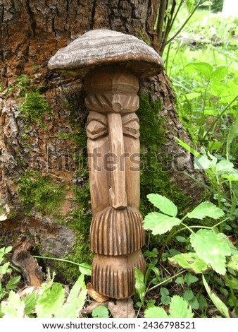 A homemade wooden figurine (the property of the author of the photo) an old man or a fairy-tale character, an idol, stands in the garden by the trunk of a tree.
