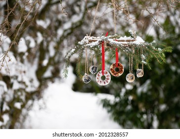 Homemade Wreath With Donut And Mini Bundt Suet Cakes Hanging In The Snowy Winter Garden. Feeding The Birds In Winter. Copy Space.