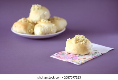 Homemade Yeast Roll (bun) With Crumble On A Flowery Napkin. Pleasant Gray - Violet Background, In The Distance A Plate With Buns. Copy Space.