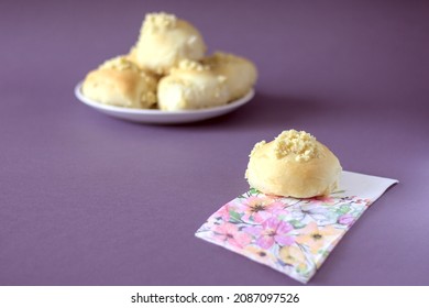 Homemade Yeast Roll (bun) With Crumble On A Flowery Napkin. Pleasant Gray - Violet Background, In The Distance A Plate With Buns. Copy Space.