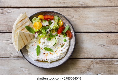 Homemade yogurt cheese (labneh) with raw vegetable salad and lavash bread  served on rustic plate on natural wooden table. Flat lay. Copy space Stock-foto