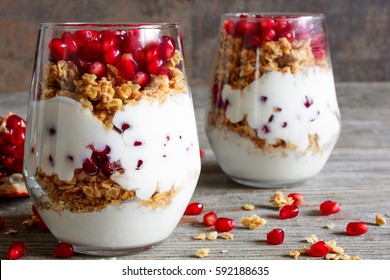 homemade yogurt parfait with granola and pomegranate fruit in glasses on rustic wooden table. healthy breakfast - Powered by Shutterstock