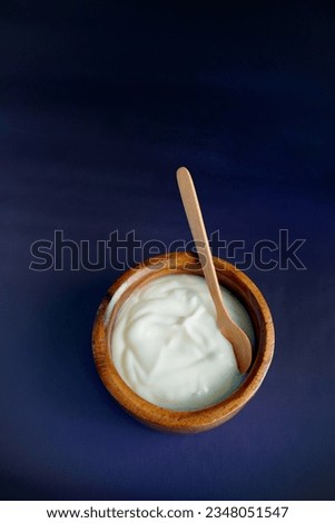 Homemade yogurt in wooden bowl with dark blue background.