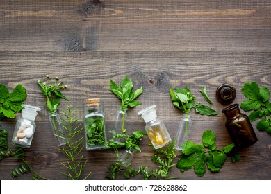 Homeopathy. Leaves of healing herbs, bottles and pills on wooden background top view copyspace