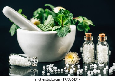 Homeopathy Treatment - Homeopathic globules scattered out of glass bottle, mortar and pestle full of fresh medicinal plants, black background