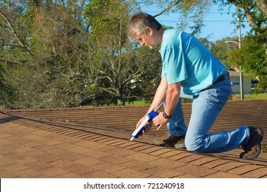 Homeowner Patching Roof With Roof Repair Tar In Caulk Gun Doing Home Maintenance To Protect And Weatherproof The House From Rain, Wind, Storms And Hurricanes.