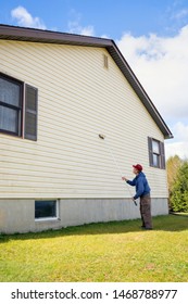 Homeowner Washing Mold From Vinyl Siding On North Side Of House With Brush And Cleaning Fluid