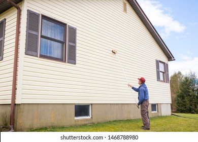 Homeowner Washing Mold From Vinyl Siding On North Side Of House With Brush And Cleaning Fluid