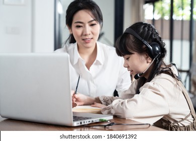 Homeschool Asian Little Young Girl Learning Online Class From School Teacher By Digital Remote Internet Meeting Due To Coronavirus Pandemic. Kid Looking Computer And Writing Note, Sitting With Mother.