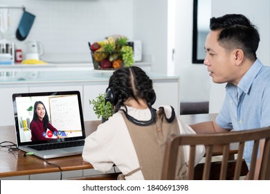 Homeschool Asian Little Young Girl Learning Online Class From School Teacher By Digital Remote Internet Meeting Due To Coronavirus Pandemic. Kid Looking Computer Laptop Screen Sitting With Father.