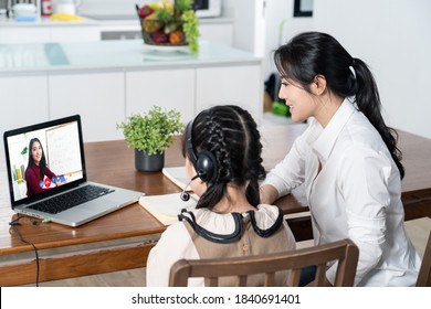 Homeschool Asian Little Young Girl Learning Online Class From School Teacher By Digital Remote Internet Meeting Due To Coronavirus Pandemic. Kid Looking Computer Laptop Screen Sitting With Mother.