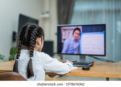 Homeschool Asian Little Young Girl Learning Online Class From School Teacher By Digital Remote Meeting Due Covid19 Pandemic. Kid Look To Virtual Video Conference At Computer Laptop And Study In House.