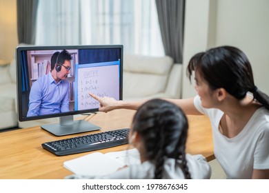 Homeschool Asian Little Young Girl Learning Online Class From School Teacher By Digital Remote Internet Meeting Due To Coronavirus Pandemic. Kid Looking Computer And Writing Note With Help From Mother