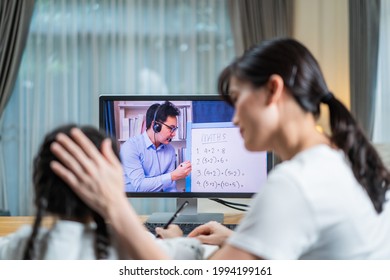 Homeschool Asian Little Young Girl Learning Online Class From School Teacher By Digital Remote Internet Meeting Due To Coronavirus Pandemic. Kid Looking Computer And Writing Note With Help From Mother