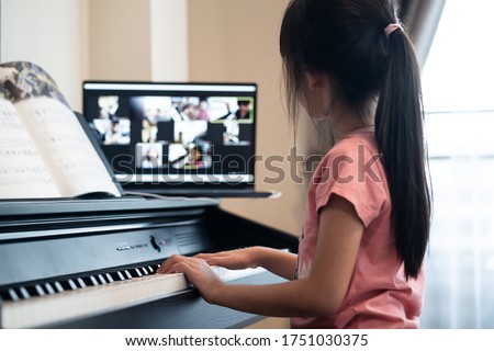 Homeschool Asian little young kid girl learning piano from computer connecting to internet music online class by school teacher. New normal lifestyle and education, student study at home concept.