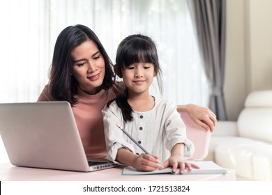 Homeschool Asian young little girl learning internet online class and do homework by using computer with mother help, teach and encourage. Daughter smile and happy to study at home together with mom.