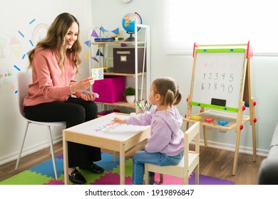 Homeschool mom teaching her little daughter how to count. Female teacher or tutor showing learning cards with numbers to an elementary girl at her home