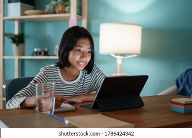 Homeschooling Asian Girl Doing Homework And Study Online With Tablet At A Desk At Night.