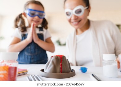 Homeschooling Concept. Mother And Daughter In Protective Glasses Having Fun Making DIY Volcano Model Eruption From Kids Play Clay For School Science Project Homework.