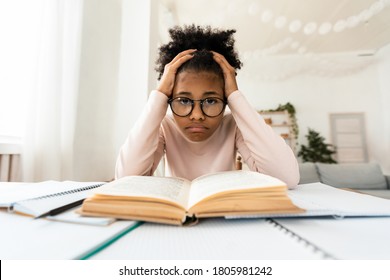 Homeschooling Depression. Frustrated Black Girl Touching Head Looking At Camera Sitting At Book Doing Homework At Home