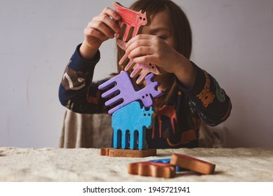 Homeschooling, Waldorf Education, Learning A Balance - Girl Builds A Balance Tower From Colored Wooden Toys: Bison, Elk, Fox And Lynx