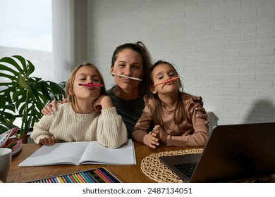 Homework fun: Mother and daughters, seated at the dining table, make silly faces while tackling homework, turning study time into a laughter-filled adventure. - Powered by Shutterstock