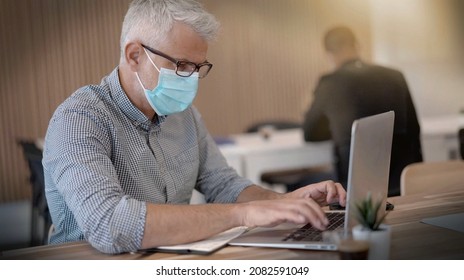 Homme portant un masque contre le covid-19 et travaillant dans un bureau - Shutterstock ID 2082591049