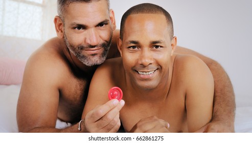 Homosexual Couple, Happy Gay People Smiling At Camera. Hispanic Friends In Bedroom Showing Condom For Safe Sex.
