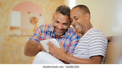 Homosexual Couple, Hispanic Gay Men Laughing While Looking At Pictures On Tablet Pc At Home