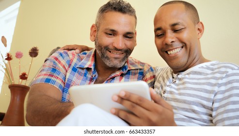 Homosexual Couple, Hispanic Gay Men Hugginh While Looking At Pictures On Tablet Pc At Home