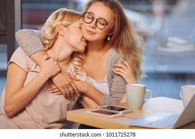Homosexual couple. Joyful peaceful young women sitting together at the table and hugging each other while being in love - Shutterstock ID 1011725278