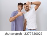 Homosexual gay couple standing over white background smiling making frame with hands and fingers with happy face. creativity and photography concept. 