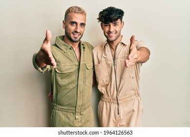 Homosexual Gay Couple Standing Together Wearing Casual Jumpsuit Smiling Friendly Offering Handshake As Greeting And Welcoming. Successful Business. 