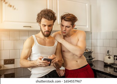 Homosexual Married Gay Couple Stand In Kitchen At Morning, Two Men Using Mobile Phone, Looking For Profitable Mortgage, They Want To Equip Life Together