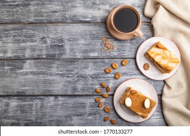 Honey Cake With Milk Cream, Caramel, Almonds And A Cup Of Coffee On A Gray Wooden Background And Linen Textile. Top View, Flat Lay, Copy Space.