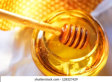 Honey Dipper On The Bee Honeycomb Background. Honey Tidbit In Glass Jar And Honeycombs Wax.