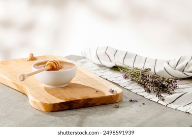 Honey with honey dipper in white bowl on wooden board and kitchen cloth and lavender on a table. White wall with natural sunlight background and copy space for products. - Powered by Shutterstock