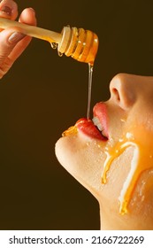 Honey dripping from honey dipper on sexy girl lips. Thick honey dipping from the wooden honey spoon. Beauty model woman open mouth, model eating nectar. Healthy food concept, diet, dessert. 