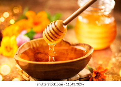 Honey dripping from honey dipper in wooden bowl.  Close-up. Healthy organic Thick honey dipping from the wooden honey spoon, closeup. Sweet dessert background