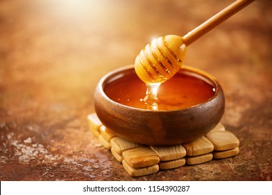 蜂蜜滴从蜂蜜浸泡在木碗。 特写。 健康的有机厚蜂蜜浸渍从木蜂蜜勺，特写。
