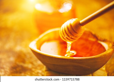 Honey dripping from honey dipper in wooden bowl.  Close-up. Healthy organic Thick honey pouring from the wooden honey spoon, closeup.