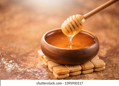 Honey dripping from honey dipper in wooden bowl.  Close-up. Healthy organic Thick honey dipping from the wooden honey spoon, closeup
