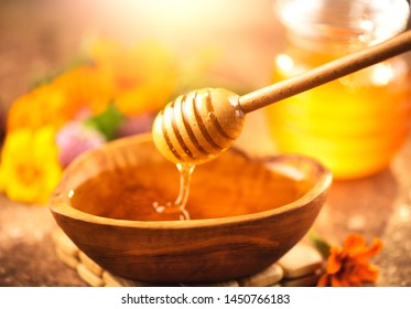 Honey dripping from honey dipper in wooden bowl.  Close-up. Healthy organic Thick honey dipping from the wooden honey spoon, closeup. Cure. Alternative medicine. Sweet dessert background