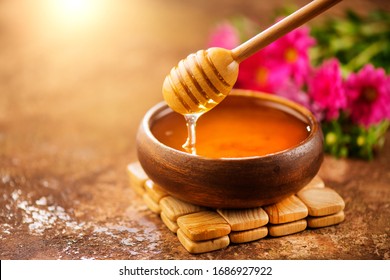 蜂蜜从木碗里的北斗七星上滴下来。特写。从木制蜂蜜勺中浸出的健康有机浓稠蜂蜜，特写。 
