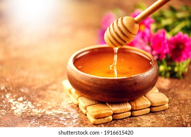Honey dripping from honey dipper in wooden bowl.  Close-up. Healthy organic thick honey dipping from the wooden honey spoon, closeup   - Shutterstock ID 1916615420
